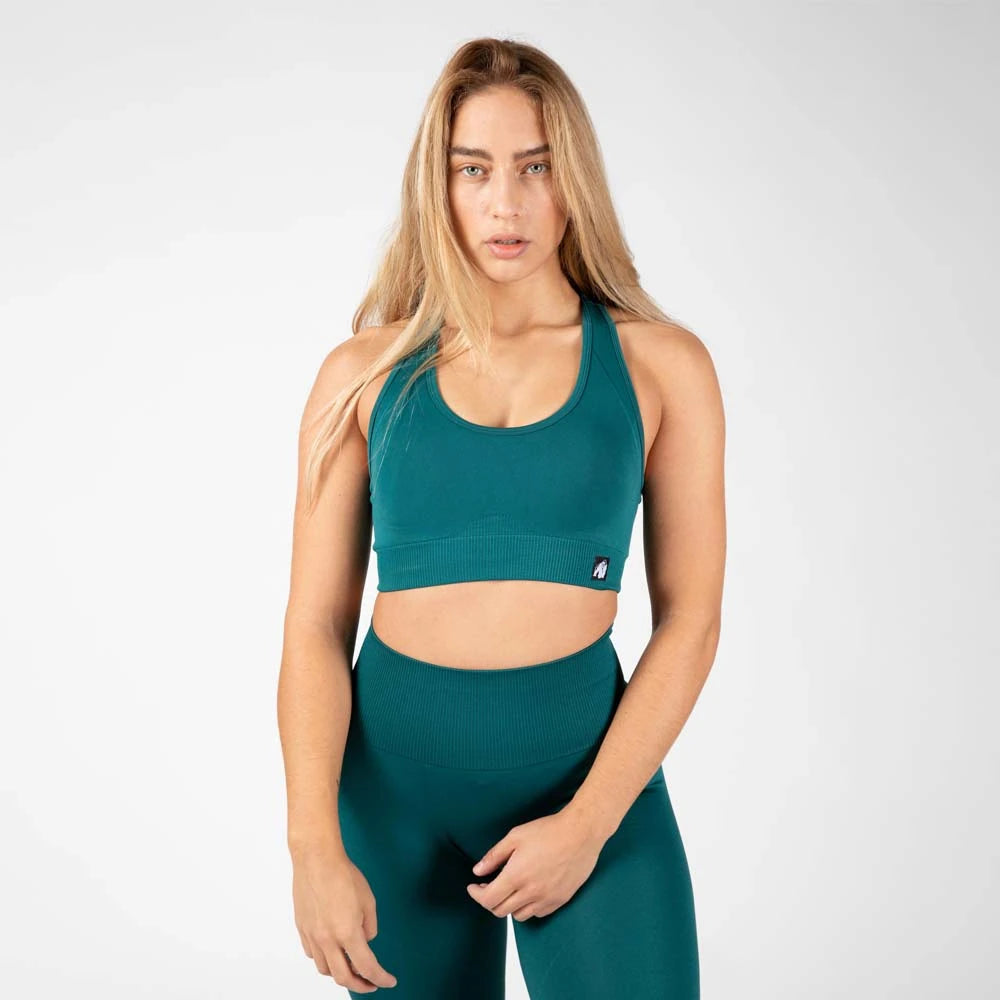 Gorilla Wear Yava Seamless Sport Bra Green, en sømløs grønn sports-BH med bred ribbestrikket linning båret av en kvinne.