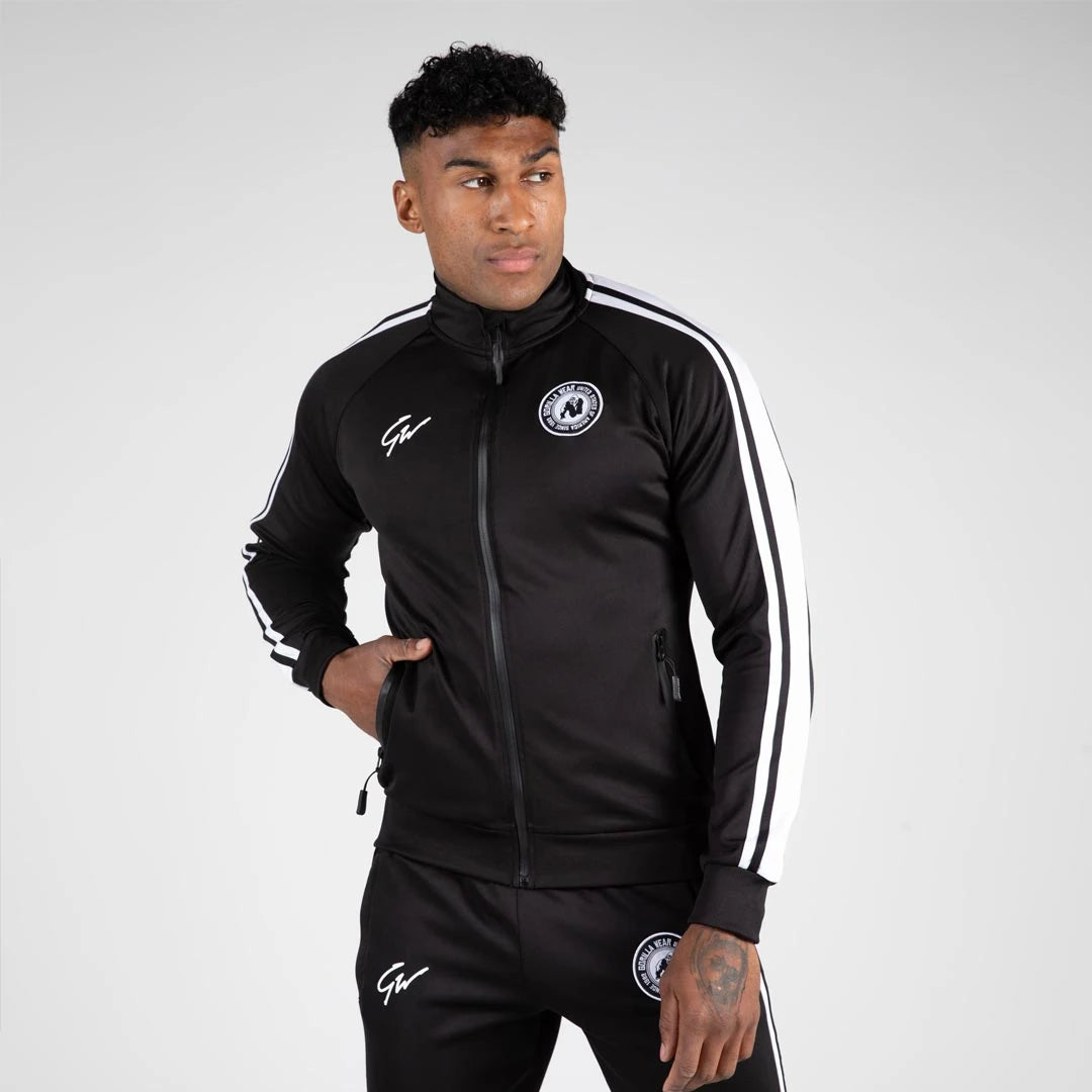 Gorilla Wear Stratford Track Jacket Black er en svart treningsjakke med hvite striper og glidelås, båret av en mann., bilde 3 av 6