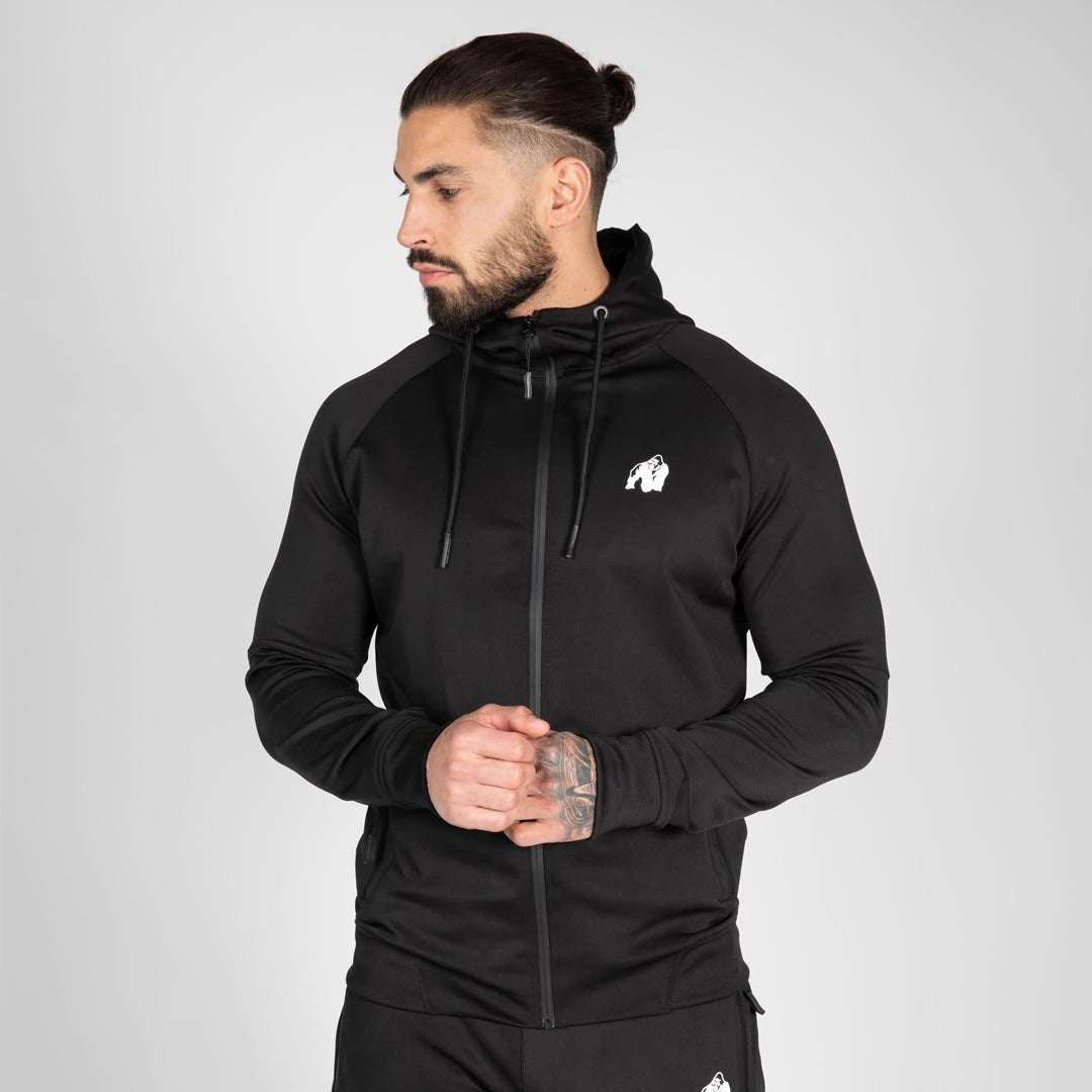 Gorilla Wear Sullivan Track Jacket Black, en svart treningsjakke med hette og hvit logo båret av en mann., bilde 6 av 7