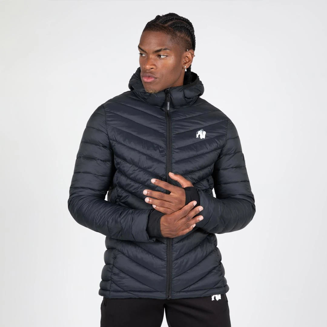 Mann i Gorilla Wear Osborn Puffer Jacket Black, en svart vattert slim fit-jakke med hette og tommelhull., bilde 1 av 8