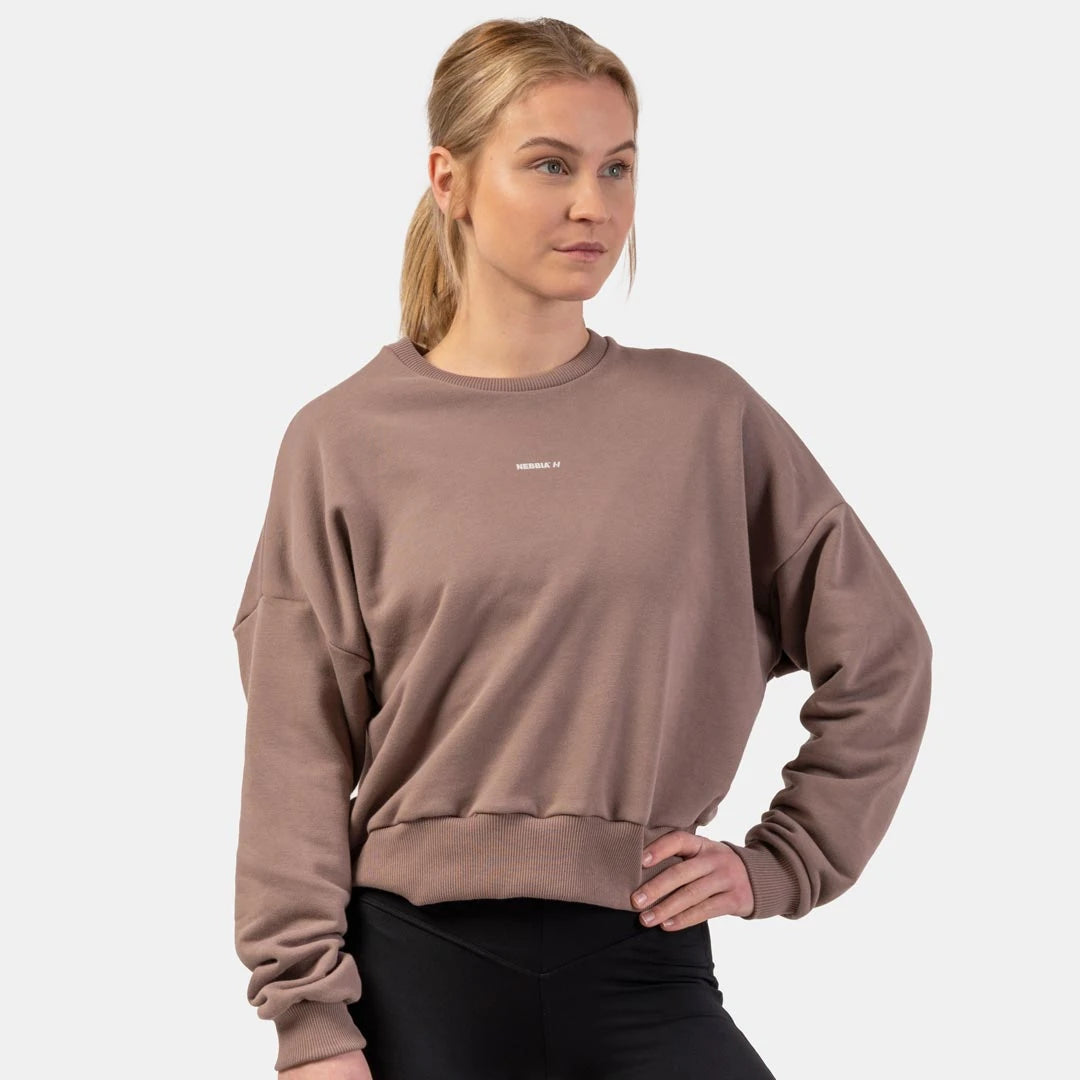 NEBBIA Loose Fit Sweatshirt Feeling Good Brown, en brun treningsgenser med løs passform og brede mansjetter på en kvinne., bilde 2 av 3