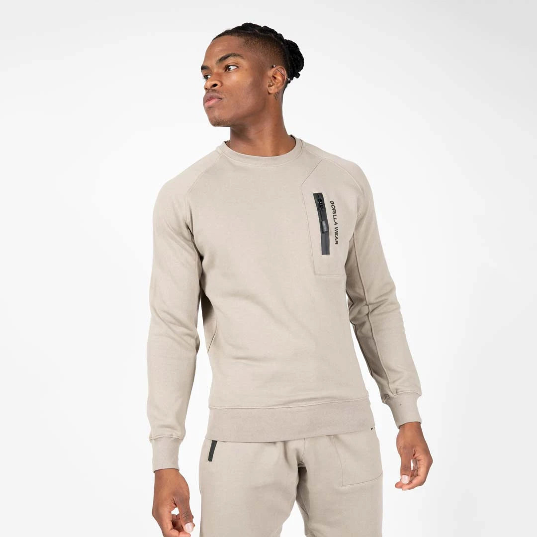 Gorilla Wear Newark Sweater Beige på en mannlig modell, en avslappet treningsgenser med svart brystlomme og glidelås.
