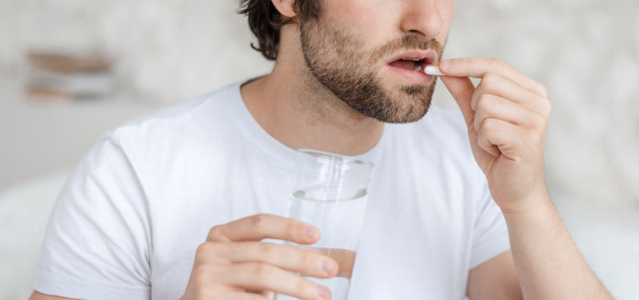 En mann som holder et glass med vann og tar vitamin-tilskudd